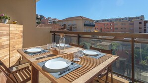 A wooden balcony table set with plates, glasses, and cutlery, overlooking a residential area with colorful buildings. - Saint James by Interhome (Le Lavandou)