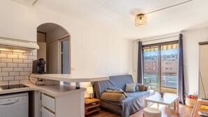 A compact living space with a kitchenette, a sofa bed, a dining table, and a large window offering a city view. - Saint James by Interhome (Le Lavandou)