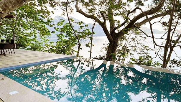 A swimming pool with a wooden deck and a large tree in the background. - El Nido Water Front (El Nido)