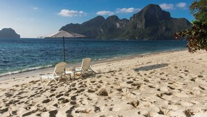 A beach with white lounge chairs and a table, clear blue water, and a mountainous backdrop. - El Nido Water Front (El Nido)