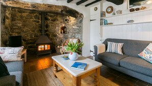 A cozy living room with a stone fireplace, a sofa, a coffee table with a book, and a vase with flowers. - Hen Dafarn -  an on the beach that sleeps 5 guests  in 3 bedrooms (Nefyn)