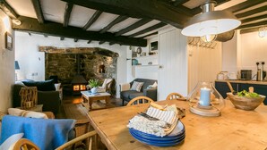 A cozy living room with a stone fireplace, wooden furniture, and a dining area with a table set for a meal. - Hen Dafarn -  an on the beach that sleeps 5 guests  in 3 bedrooms (Nefyn)