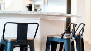 Un coin cuisine doté d’un plan de travail en marbre, de tabourets de bar noirs et d’un mur blanc.