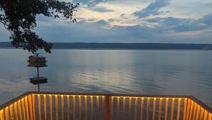 A wooden deck with two Adirondack chairs facing a calm lake at dusk. - Stunning cottage on Cayuga Lake, near wineries, waterfalls, Cornell University  (Interlaken)