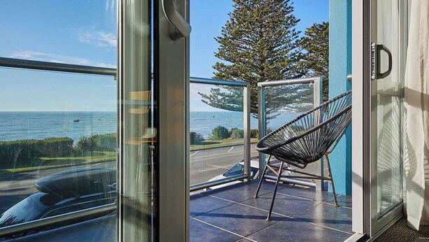 A balcony with a chair, a view of the sea, and a tree. - Kaikoura Luxury Apartments (Kaikoura)
