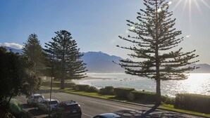 A coastal road with parked cars, trees, and a view of the ocean and mountains. - Kaikoura Luxury Apartments (Kaikoura)