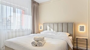 Un lit bien fait, avec des serviettes pliées, une table de chevet et un luminaire fixé au mur.