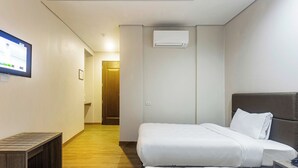 Una habitación de hotel con dos camas, un banco de madera, un televisor y un equipo de aire acondicionado.