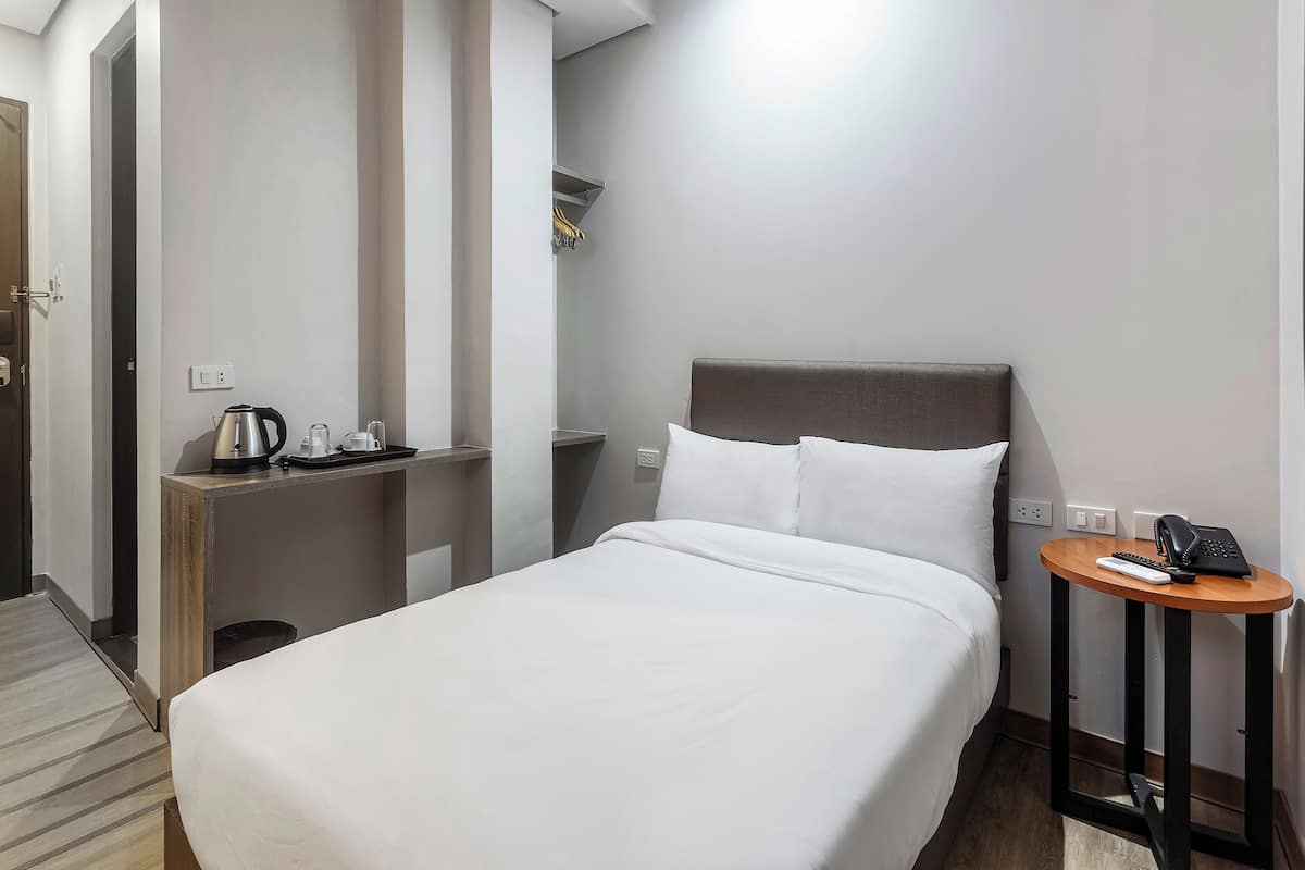 A hotel room with a single bed, bedside table, and a small round table with a phone and remote control.