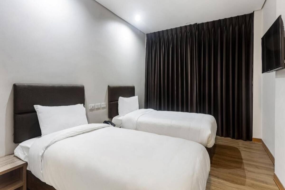 A hotel room with two beds, a flat-screen TV, and a large window with curtains.