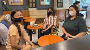 Una cafetería con mesas y sillas de madera, un panel con la carta y una zona de estar con un banco.
