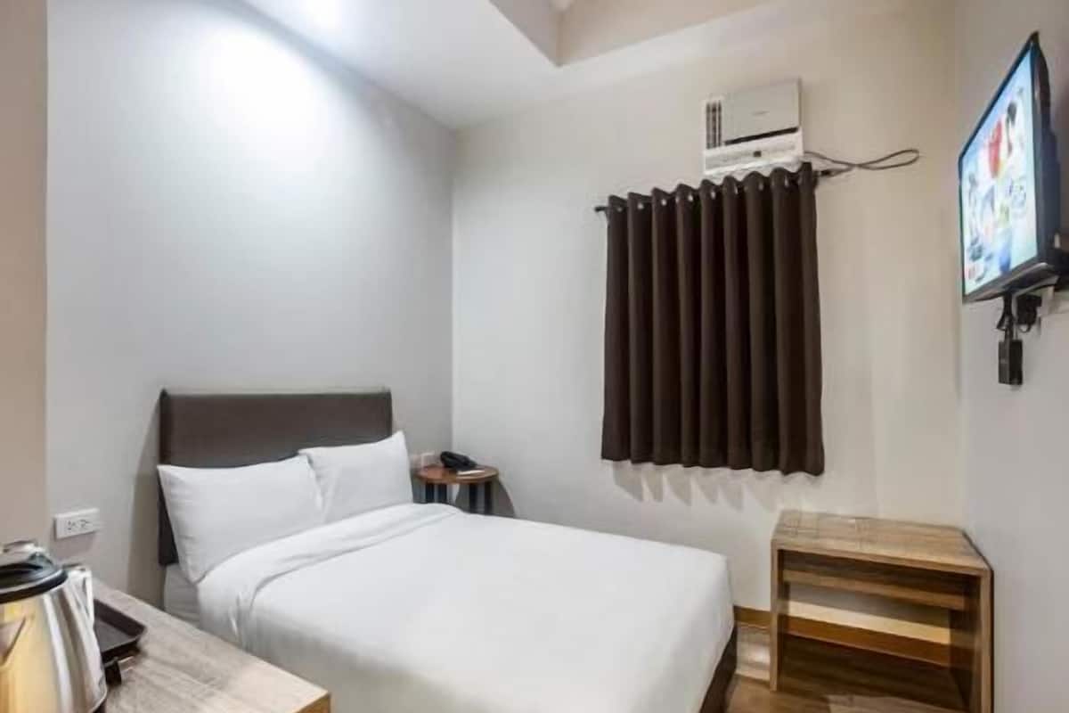 A hotel room with a bed, a bedside table, a TV, and an air conditioning unit.