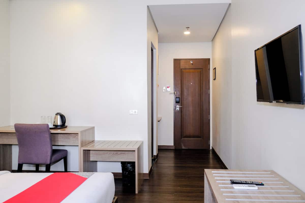 A hotel room with a bed, a desk with a chair, a small table with a remote control, and a TV mounted on the wall.