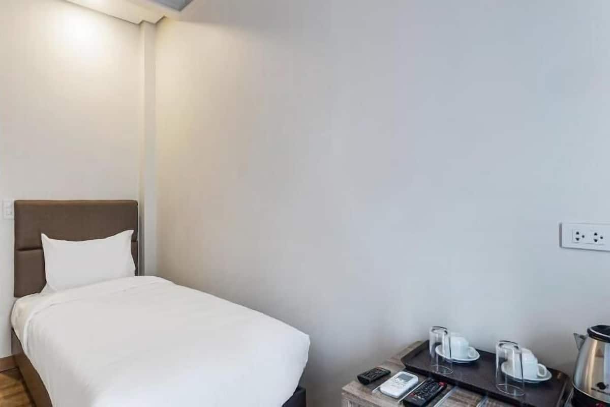 A hotel room with a bed, a bedside table with a phone and a kettle, and a door leading to another room.