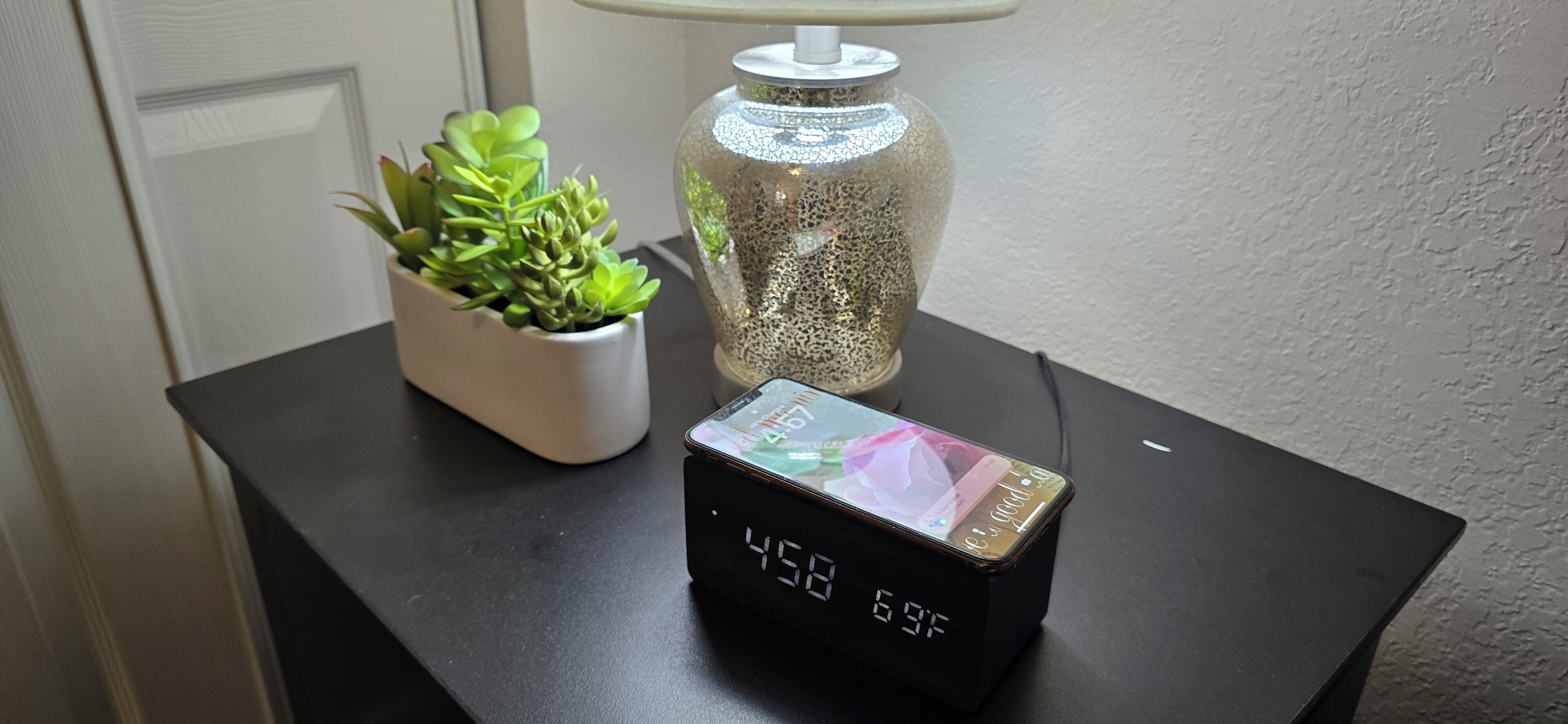 Une horloge numérique affichant 4 h 58 et 6 h 59, une plante en pot et un vase en verre décoratif, le tout posé sur une table noire.