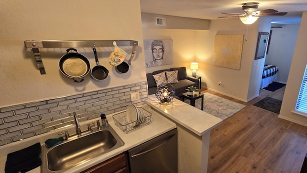A kitchen with a sink, stove, and hanging pots. There is a dining area with a table and chairs, and a living room with a couch and a Buddha statue. - Cozy Updated Cove of Heaven, 5 mins from Lake Hefner and mall. Centrally located (Oklahoma City)