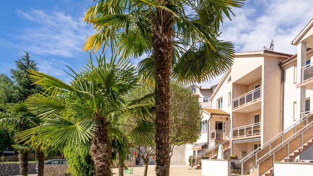 A courtyard with palm trees, a stone wall, and a building with balconies and a staircase. - Apartment Palms by Interhome (Opatija/Pobri)