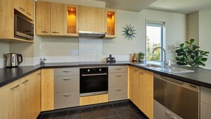 A modern kitchen with wooden cabinets, stainless steel appliances, and a window providing natural light. - Kaikoura Luxury Apartments (Kaikoura)
