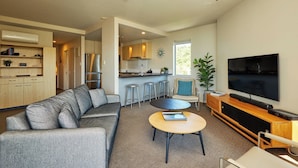 A modern living room with a grey sofa, a round coffee table, and a TV on a wooden stand. - Kaikoura Luxury Apartments (Kaikoura)
