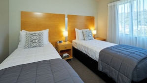 A hotel room with two beds, each with a headboard, bedside tables, and lamps. - Kaikoura Luxury Apartments (Kaikoura)