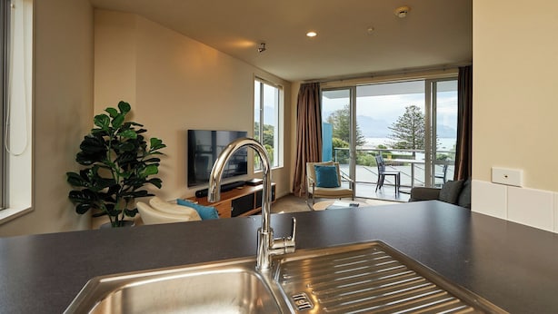 A modern kitchen with a stainless steel sink, a flat-screen TV, and a large window overlooking a scenic view. - Kaikoura Luxury Apartments (Kaikoura)