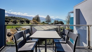 A balcony with a table and chairs, overlooking a scenic view of mountains and a lake. - Kaikoura Luxury Apartments (Kaikoura)