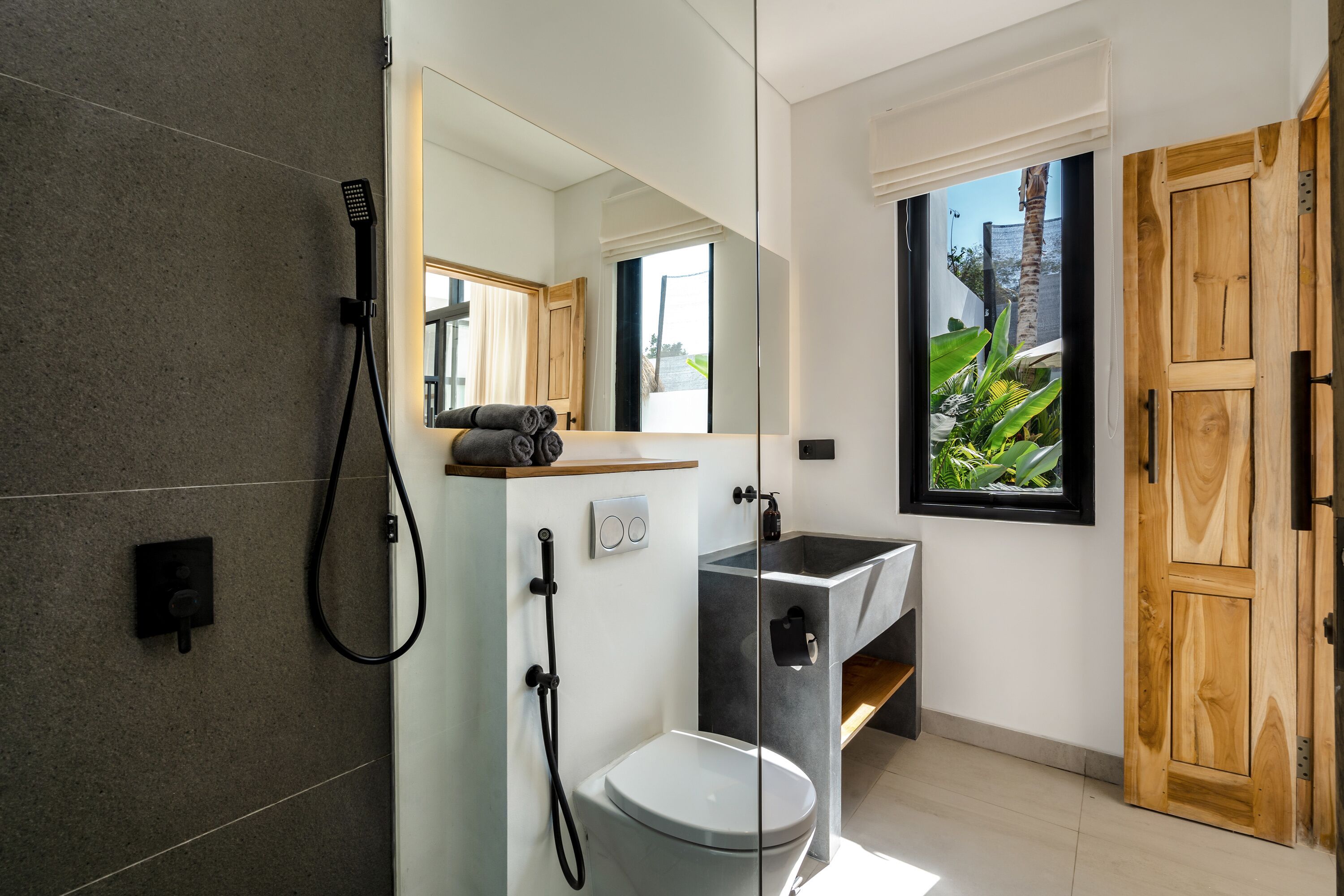 A modern bathroom with a large mirror, a shower, a toilet, and a sink.