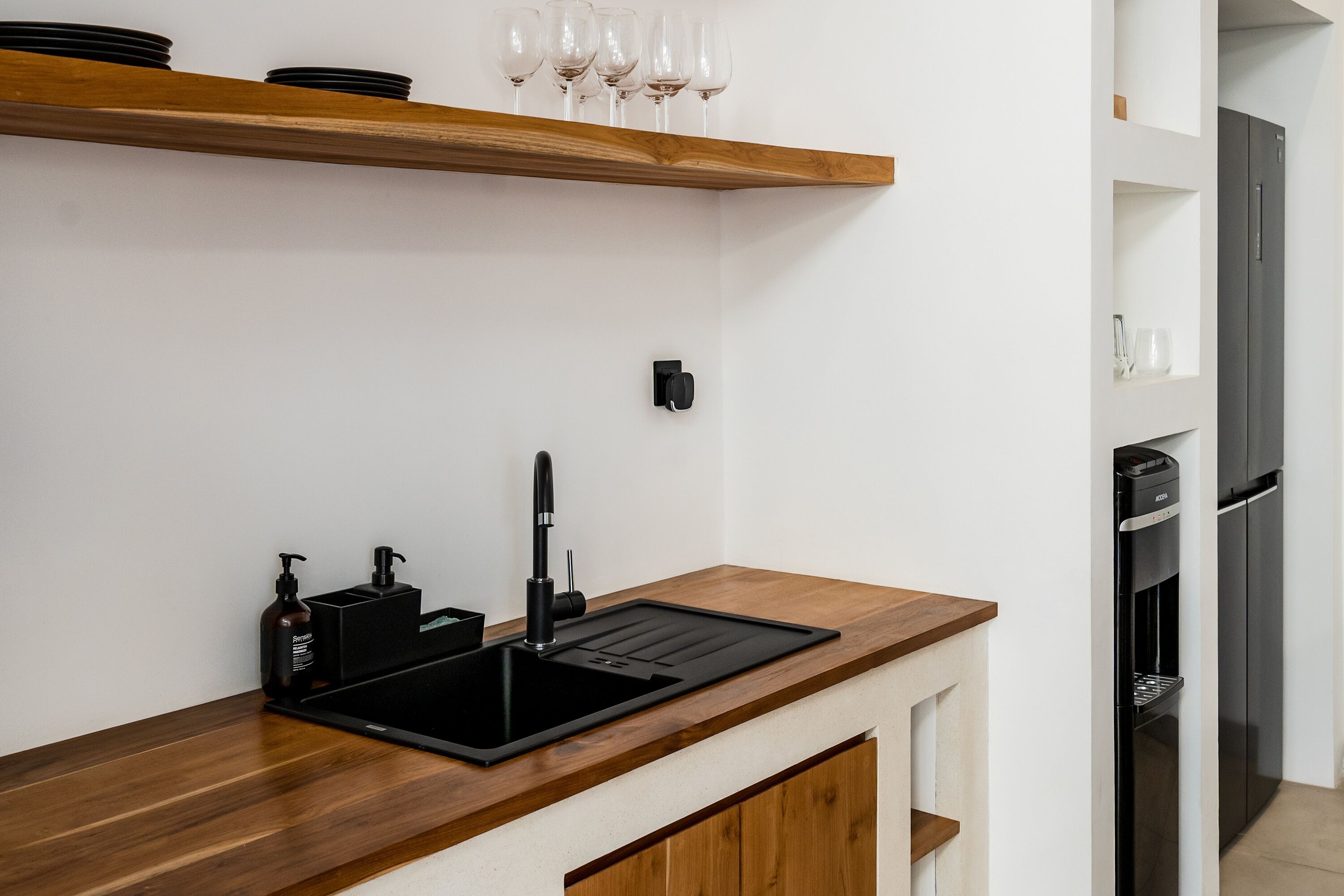 Een moderne keuken met een zwarte spoelbak, een houten aanrechtblad en een inbouw wijnrek.