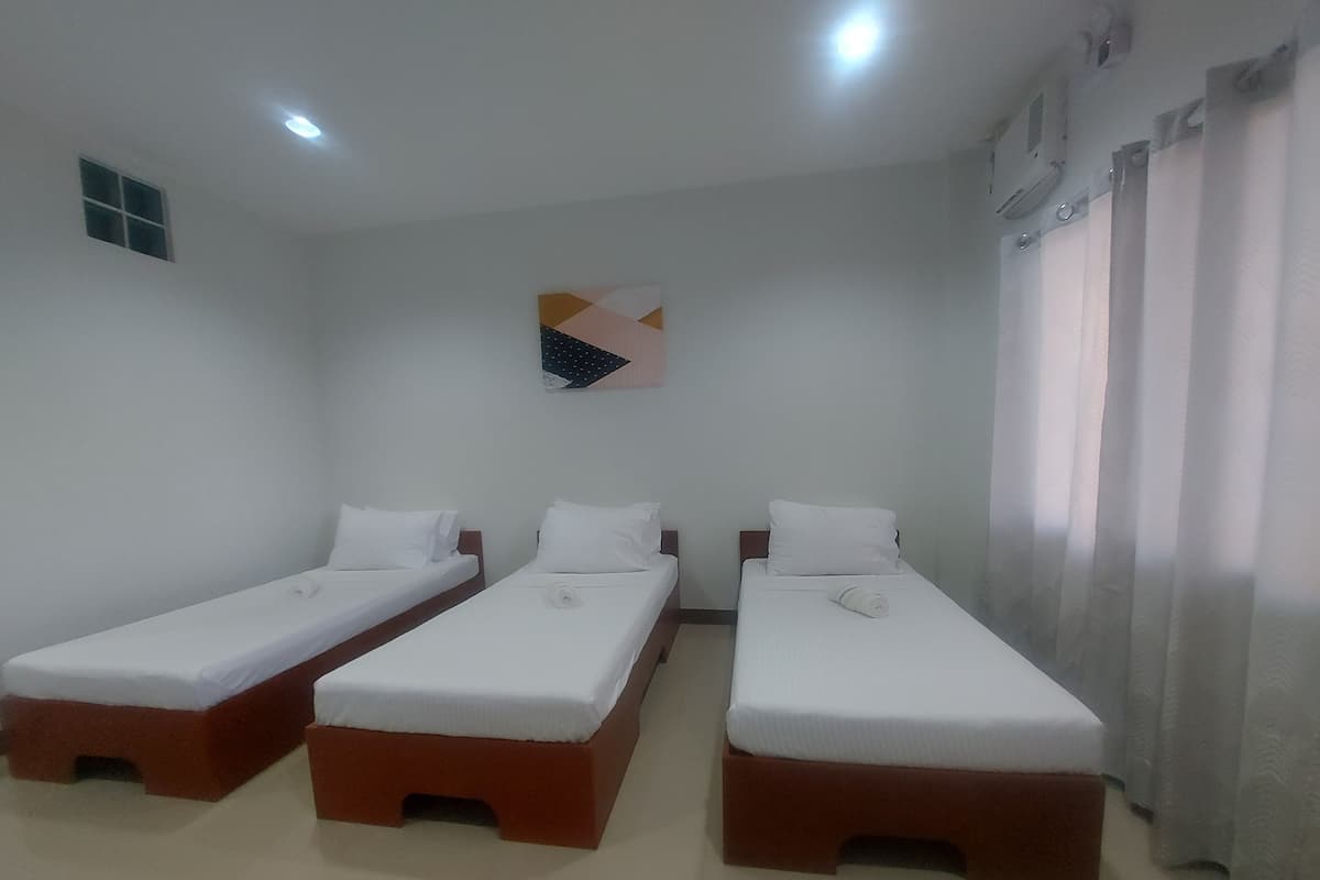 A hotel room with three single beds, a small window, and a ceiling light.