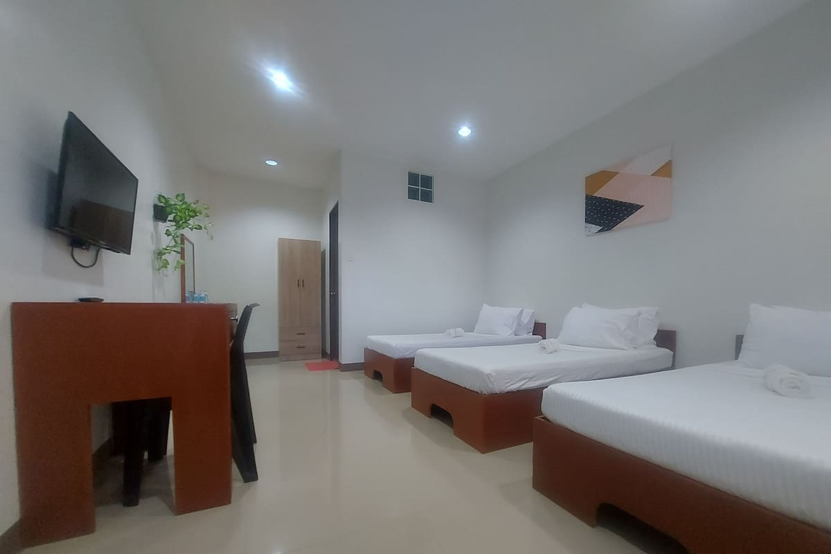 A hotel room with three single beds, a desk with a chair, a TV, and a wardrobe.