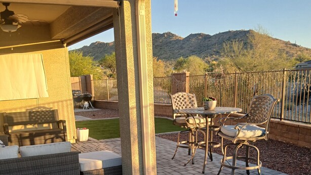 An outdoor patio with a covered seating area, a table with chairs, and a view of a hilly landscape. - Peaceful home in Estrella Mountains with beautiful lake for walking  (Goodyear)