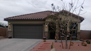 A residential house with a garage, a driveway, and a landscaped garden with cacti and rocks. - Peaceful home in Estrella Mountains with beautiful lake for walking  (Goodyear)