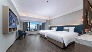 Una habitación de hotel moderna con dos camas, un escritorio y un amplio ventanal con vistas a la ciudad.