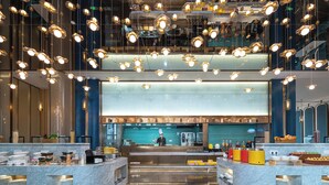 Un moderno vestíbulo de hotel con una recepción central, una cocina grande con azulejos azules al fondo y un suelo de mármol.