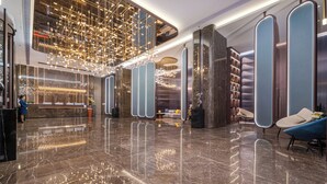 Un lobby moderno con suelo de mármol, una recepción, zonas de estar e iluminación decorativa en el techo.