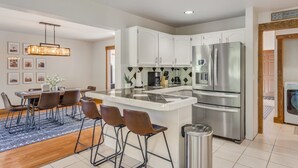 Une cuisine moderne avec des meubles blancs, un réfrigérateur en acier inoxydable et un coin repas comprenant une table et des chaises.