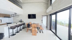 A modern kitchen with a bar area, a dining table with chairs, and a large window offering a view. - Ocean view retreat! Luxury villa with sauna (本部町)