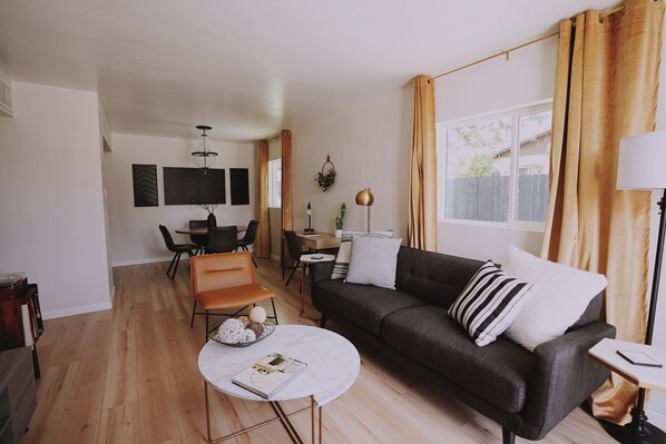 A modern living room with a dark grey sofa, a round coffee table, and a dining area with a table and chairs. - The White House.  Stylish Uptown Retreat near Dining & Shopping (Albuquerque)