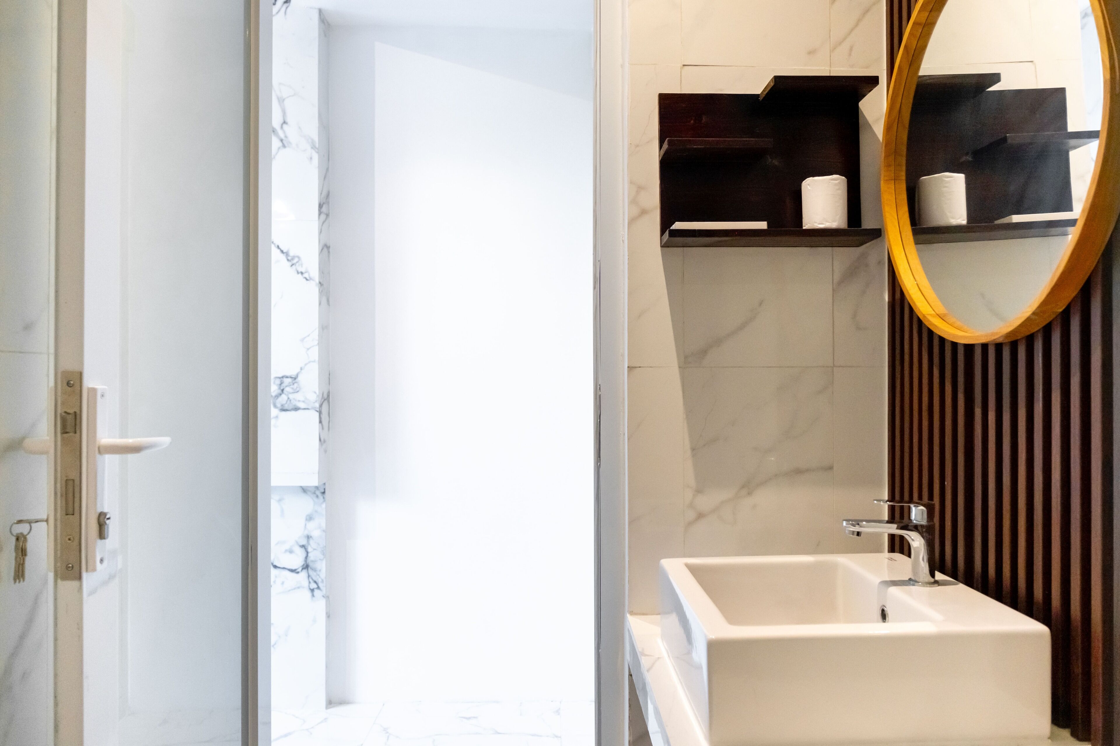 A modern bathroom with a white sink, a mirror with a wooden frame, and marble-patterned walls.