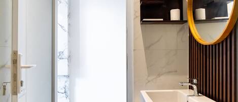 A modern bathroom with a white sink, a mirror with a wooden frame, and marble-patterned walls.