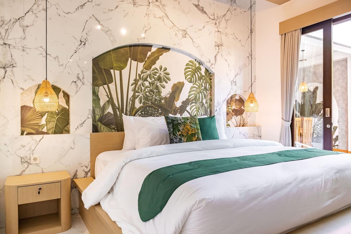 A hotel room with a marble wall, a bed with white bedding and a green throw, a wooden nightstand, and two wall-mounted lamps.