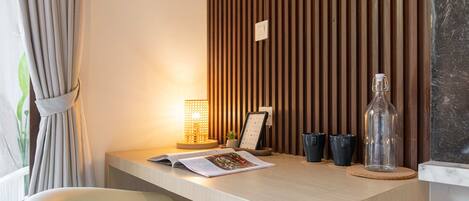 A modern hotel room with a wooden desk, a lamp, a magazine, and a bottle.