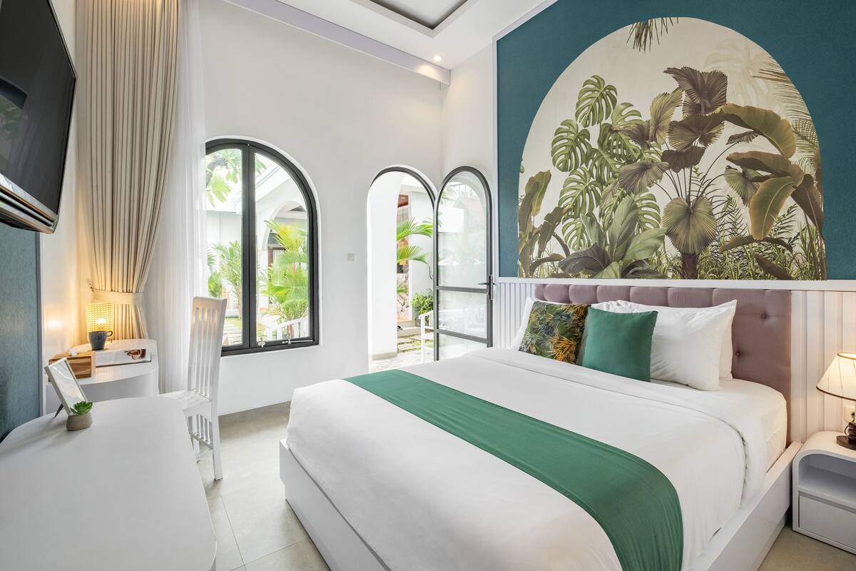 A modern hotel room with a large bed, a desk, and a mural of tropical plants.