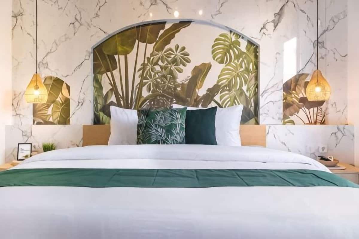 A bed with a green bedspread, a headboard with a plant mural, and two bedside lamps.