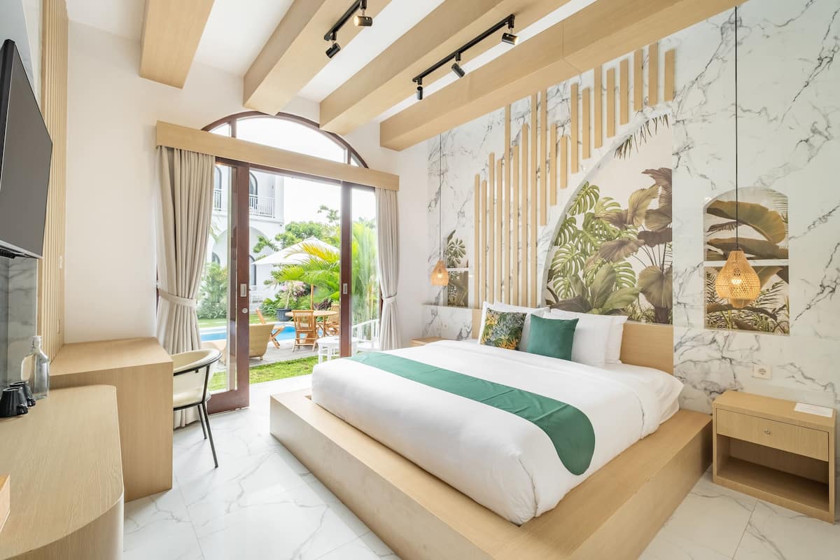 A modern hotel room with a large bed, a desk, and a view of the garden.