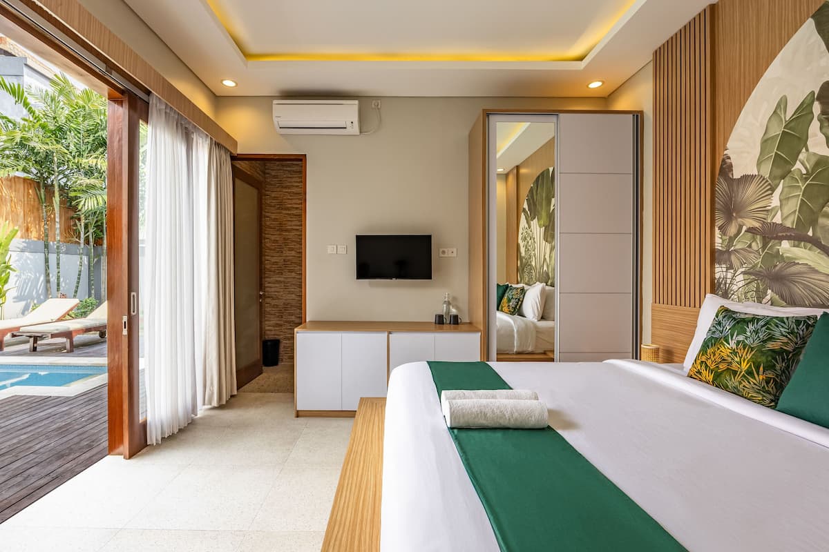 A modern hotel room with a bed, a TV, a desk, and a view of a pool.