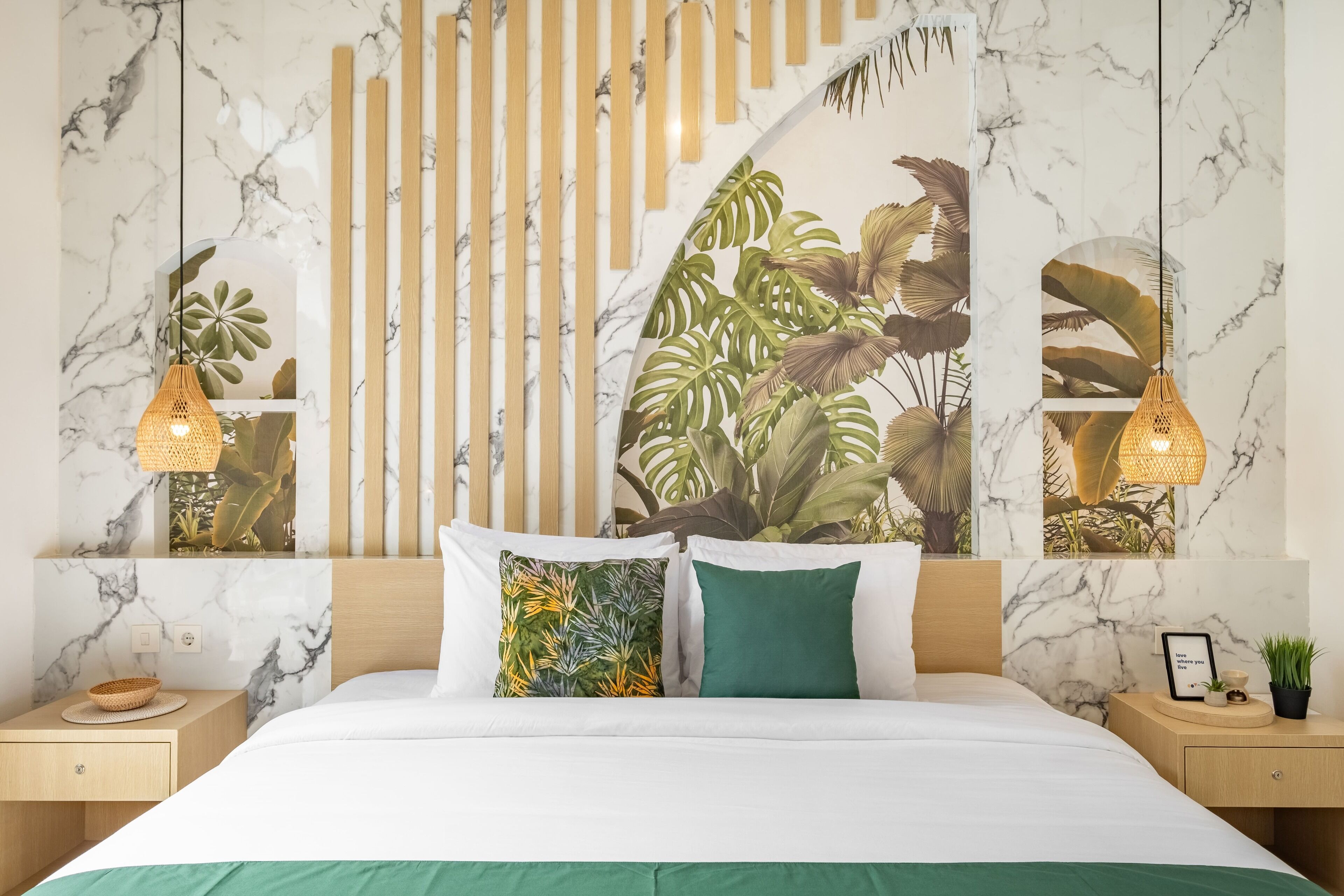 Une chambre avec un lit, deux tables de chevet, un mur orné d’un motif en marbre, un mur avec des lambris en bois et une fresque représentant des plantes tropicales.