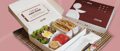 A meal box with a sandwich, salad, and yogurt, and a separate box with a logo.