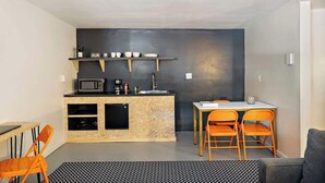 Cocina compacta con microondas, cafetera y lavabo. Un pequeño comedor con dos sillas color naranja y una mesa.