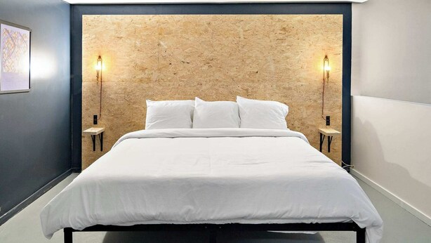 Una habitación de hotel moderna con una cama grande, dos mesitas de noche y un cabecero de madera.